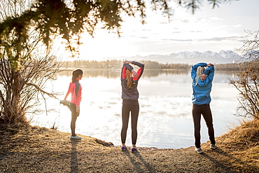 Three young women stretching on a trail at the water's edge, Anchorage, Alaska, United States of America