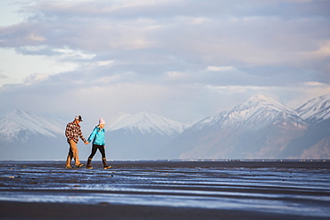 A young couple walking on a beach and holding hands with a mountain range in the distance, Anchorage, Alaska, United States of America