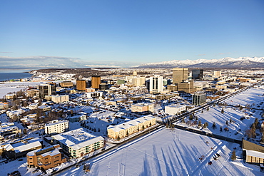 Aerial view of snow covering downtown Anchorage and the Chugach and Talkeetna Mountains stretching out behind the city in the distance, the Park Strip visible in the foreground, South-central Alaska in winter, Anchorage, Alaska, United States of America