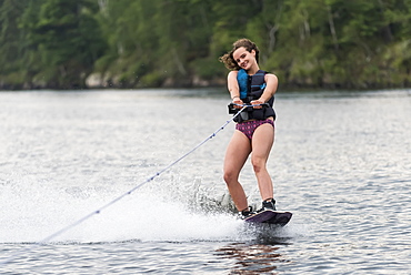 A teenage girl wakeboarding behind a boat on a lake, Lake of the Woods, Ontario, Canada