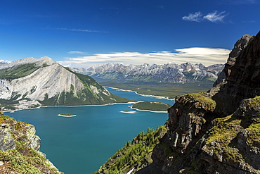 View from the top of mountain ridge looking down on colourful alpine lake and mountain range in the distance with blue sky and clouds, Kananaskis Country, Alberta, Canada