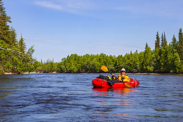 Female packrafter relaxing on a mellow stretch of the Charley River, Yukon–Charley Rivers National Preserve, Alaska, United States of America