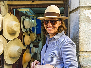 Female tourist looks at the camera and tries on a hat in a hat shop, Havana, Cuba