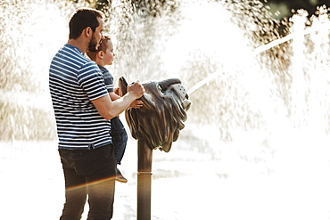 Father and young son at spray park, Edmonton, Alberta, Canada