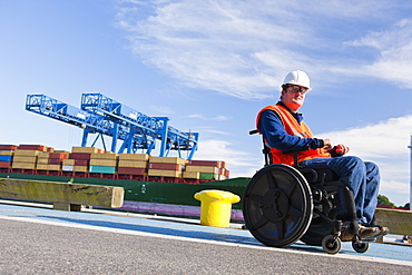 Transportation engineer in wheelchair passing bollard at shipping port