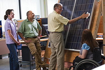 Engineering students watching professor cleaning photovoltaic panel to demonstrate improvement in efficiency