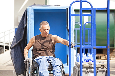 Loading dock worker with spinal cord injury in a wheelchair moving a hand truck