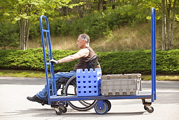 Loading dock worker with spinal cord injury in a wheelchair moving a hand truck