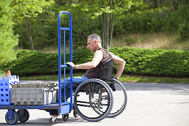 Loading dock worker with spinal cord injury in a wheelchair moving a hand truck