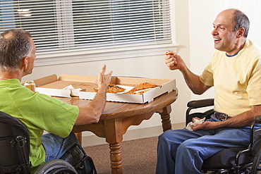 Two disabled men sitting in wheelchairs and eating pizza