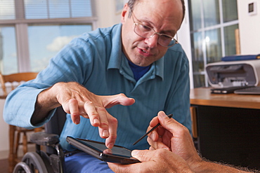 Two disabled men sitting in wheelchairs and using a digital tablet, one with deformed hands