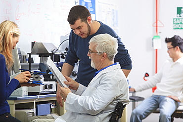 Professor with muscular dystrophy and engineering students using manual to set up x-ray fluorescence experiment in a Laboratory