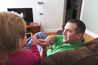 Man after anterior cruciate ligament (ACL) surgery playing with his daughter at home