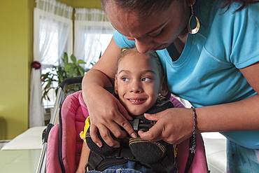 Mother strapping small daughter with Cerebral Palsy into stroller