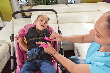 Mother putting hand brace on small daughter with Cerebral Palsy to go in stroller