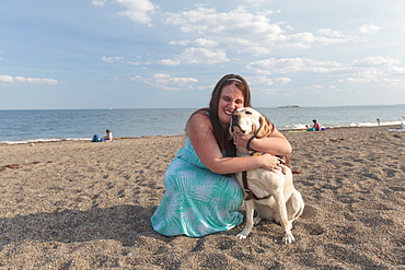 Young woman with visual impairment and her service dog hugging on the beach