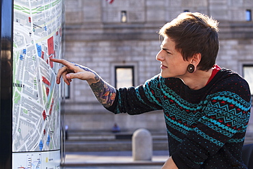 Trendy man with a spinal cord injury in wheelchair looking at a subway map of the city