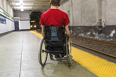 Trendy man with a spinal cord injury in wheelchair waiting for a subway train