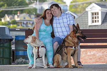 Blind couple hugging each other with their service dogs relaxing at a bench on the beach