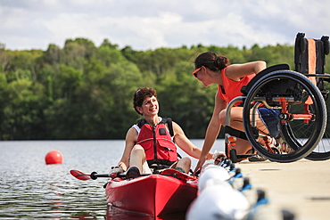 Instructor helping a woman with a Spinal Cord Injury use a kayak