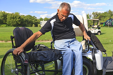 Man with spinal cord injury in an adaptive golf cart getting into his wheelchair