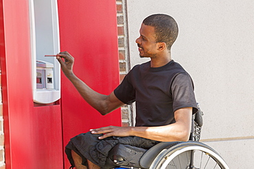 Man in a wheelchair who had Spinal Meningitis using a bank ATM