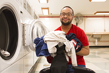 Happy African American man with Down Syndrome doing laundry in utility room