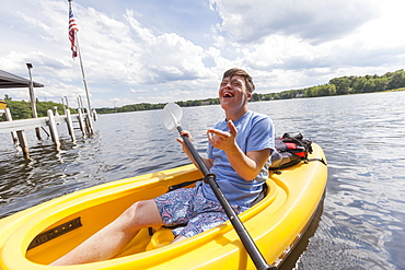 Happy young man with Down Syndrome rowing a kayak in a lake