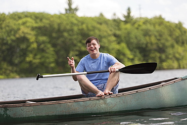 Happy young man with Down Syndrome rowing a canoe in a lake