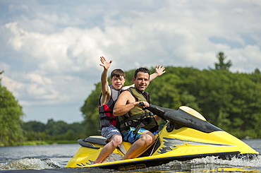 Young man with Down Syndrome riding on a jet ski with his friend in a lake