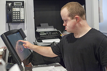 Waiter with Down Syndrome entering a sale on the computer in office