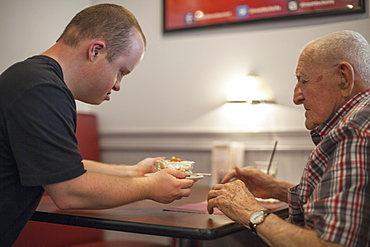 Waiter with Down Syndrome serving food to customer in a restaurant