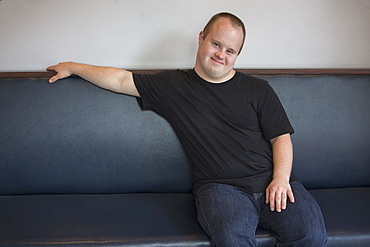 Portrait of happy waiter with Down Syndrome sitting on sofa in a restaurant