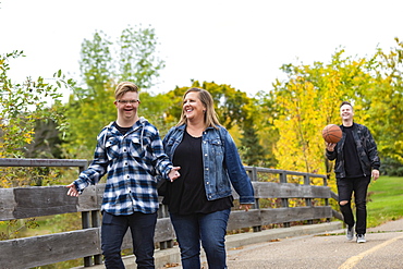 A young man with Down Syndrome walking with his father and mother while enjoying each other's company in a city park on a warm fall evening: Edmonton, Alberta, Canada