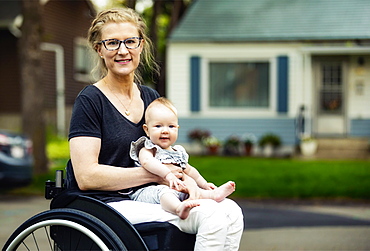 A paraplegic mom carrying her baby in her lap while using a wheelchair outdoors on a warm summer afternoon: Edmonton, Alberta, Canada