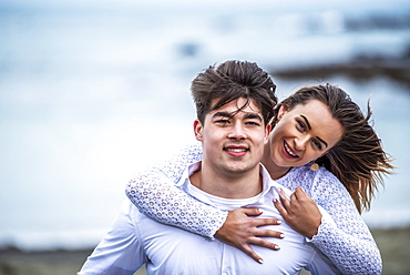 Portrait of a young couple with windblown hair on the beach; Wellington, North Island, New Zealand