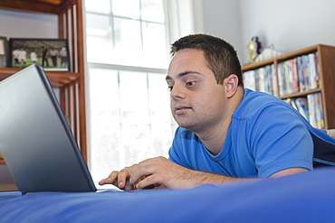 Man with Down Syndrome lying on bed using a laptop