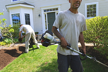 Landscapers working in a garden, one doing mulching and one doing edging with a power edger