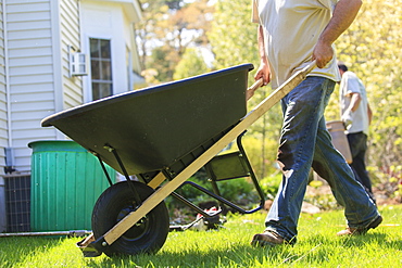 Landscaper moving wheelbarrow around a house