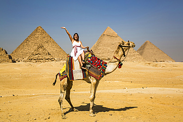 Female tourist waving while sitting on a camel, Giza Pyramid Complex, UNESCO World Heritage Site; Giza, Egypt