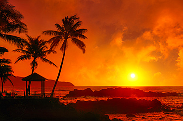 Dramatic sunrise over Uppers Beach Park with a glowing sky reflected red over the pacific ocean; Oahu, Hawaii, United States of America