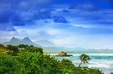 Mist over Kaupo Cove at sunrise, with a pier leading to a house and mountain peaks lining the coastline; Oahu, Hawaii, United States of America