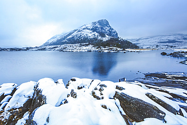 Small mountain surrounded by low clouds by one of the upper lakes in killarney with snow covered rocks in the foreground, Killarney National Park; County Kerry, Ireland