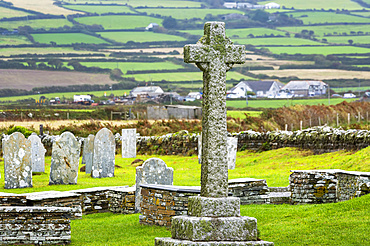 Old stone cross gravestone in graveyard with patchwork of fields in the background; Cornwall County, England