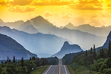 Glenn Highway divides the image, surrounded by spruce forest and brush in Southcentral Alaska, at sunset, with cars in the distance looking towards Lion's Head and the Chugach Mountains on a smokey, hazy, summer night; Chickaloon, Alaska, United States of America