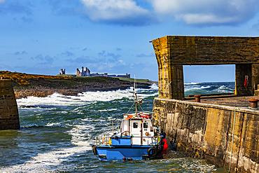 View Of Dunstanburgh Castle from a pier with a cement structure on Craster Harbour; Craster, Northumberland, England