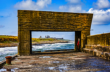 View Of Dunstanburgh Castle from a pier with a cement structure on Craster Harbour; Craster, Northumberland, England