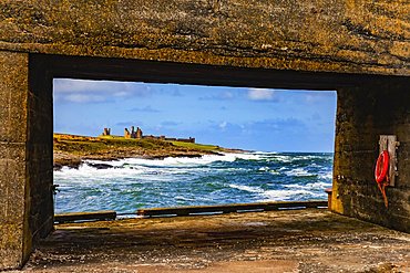 View Of Dunstanburgh Castle from a pier with a cement structure on Craster Harbour; Craster, Northumberland, England