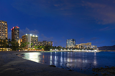 Waikiki at sunset, with illuminated buildings and tranquil waterfront; Honolulu, Oahu, Hawaii, United States of America