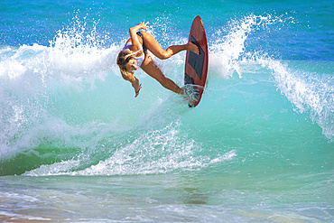 A young woman riding a wave on a skimboard off Sandy Beach, Oahu; Oahu, Hawaii, United States of America